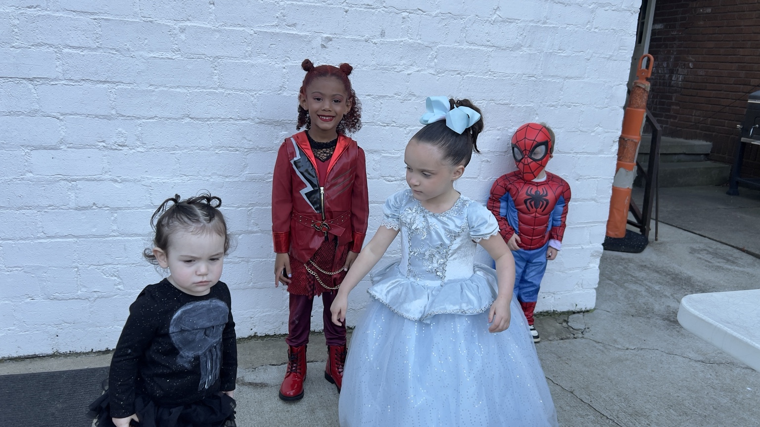 Four children together in their Halloween costumes, including a skeleton, red costume, princess, and Spider-Man